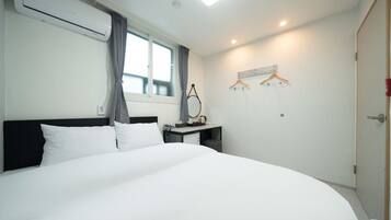 Une chambre d’hôtel avec un grand lit, un bureau avec une chaise, un porte-manteau et une fenêtre avec des rideaux.