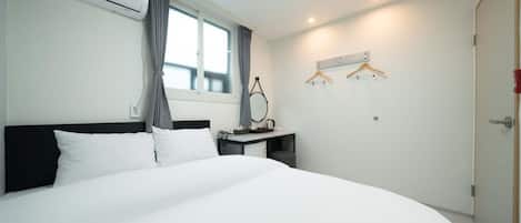 Une chambre d’hôtel avec un grand lit, un bureau avec une chaise, un porte-manteau et une fenêtre avec des rideaux.