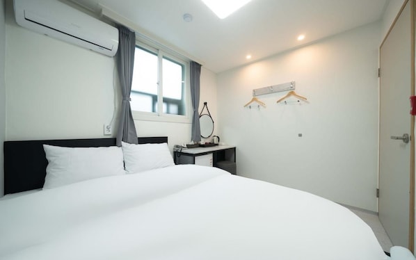 A hotel room with a large bed, a desk with a chair, a hanging coat rack, and a window with curtains.