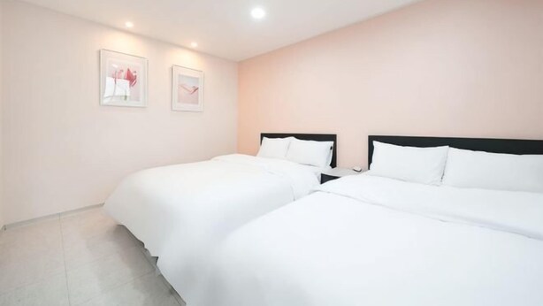 Camera da letto con due letti, arredamento bianco e due quadri appesi alle pareti.