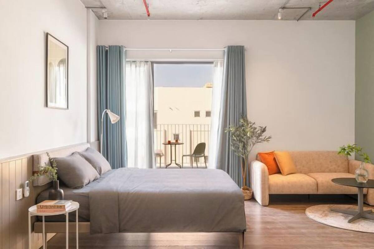 Un dormitorio con cama, sofá, una mesita y una ventana con cortinas.