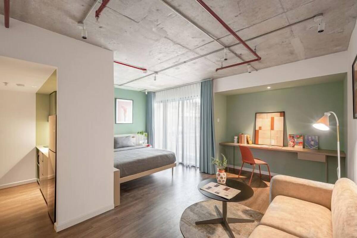 Una habitación moderna con cama, escritorio y zona de estar, que presenta techo de hormigón y suelo de madera.