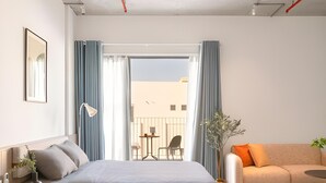 A modern hotel room with a bed, a sofa, a small table, a lamp, and a view of the outside. - Express by M Village Ky Dong, a brand of Modern Village Lifestyle (Ho Chi Minh City)