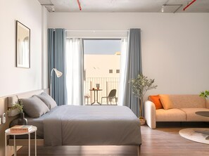 A modern hotel room with a bed, a sofa, a small table, a lamp, and a view of the outside. - Express by M Village Ky Dong, a brand of Modern Village Lifestyle (Ho Chi Minh City)