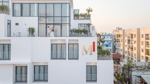 A multi-story building with a prominent 'M' sign, balconies with plants, and a view of the surrounding urban area. - Express by M Village Ky Dong, a brand of Modern Village Lifestyle (Ho Chi Minh City)