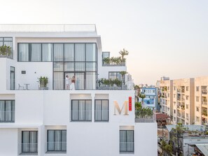 A multi-story building with a prominent 'M' sign, balconies with plants, and a view of the surrounding urban area. - Express by M Village Ky Dong, a brand of Modern Village Lifestyle (Ho Chi Minh City)
