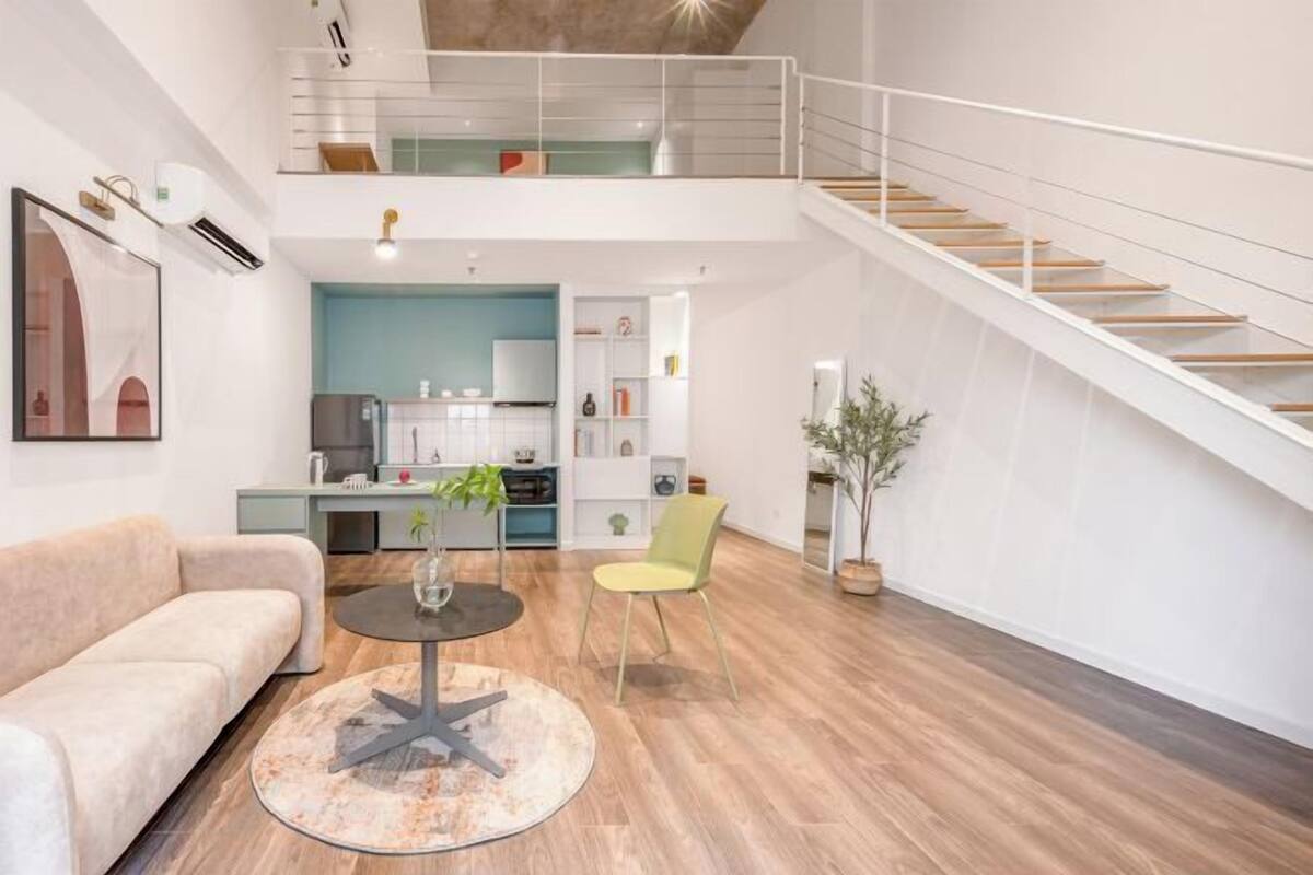 Un interior moderno con una escalera, un sofá, una mesa de comedor y una zona de cocina.