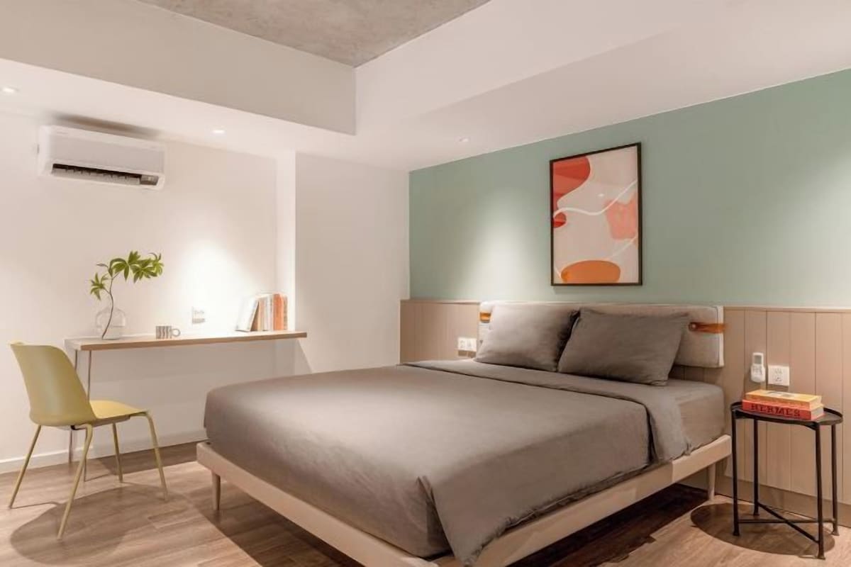 A modern bedroom with a bed, a desk, a chair, and a wall-mounted air conditioner.