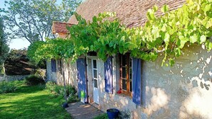 Una casa de piedra rústica con techo de tejas, un pequeño porche delantero y un jardín.