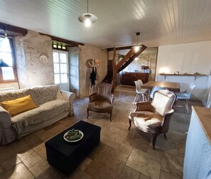 Un salon de style rustique comprenant un canapé, des fauteuils, une table basse et un coin repas avec une table et des chaises.