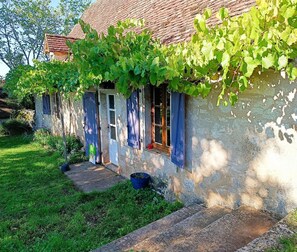 Une maison de campagne en pierre, avec un toit en tuiles, un petit porche à l’avant et un jardin.