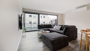 A modern living room with a sectional sofa, a round coffee table, and a wooden dining table. - Modern 3 Bedroom Townhouse - Only 10min walk to Stadium (Christchurch)