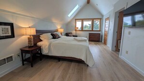 A bedroom with a bed, bedside lamps, a window, and a sloped ceiling.