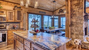 A rustic kitchen with wooden cabinets, a granite countertop, and a stone fireplace. - New! Mtn Views, pool table, fire pit (Blue Ridge)