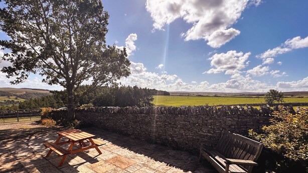 Un muro de piedra con un banco de madera y una mesa de picnic en un entorno rural.