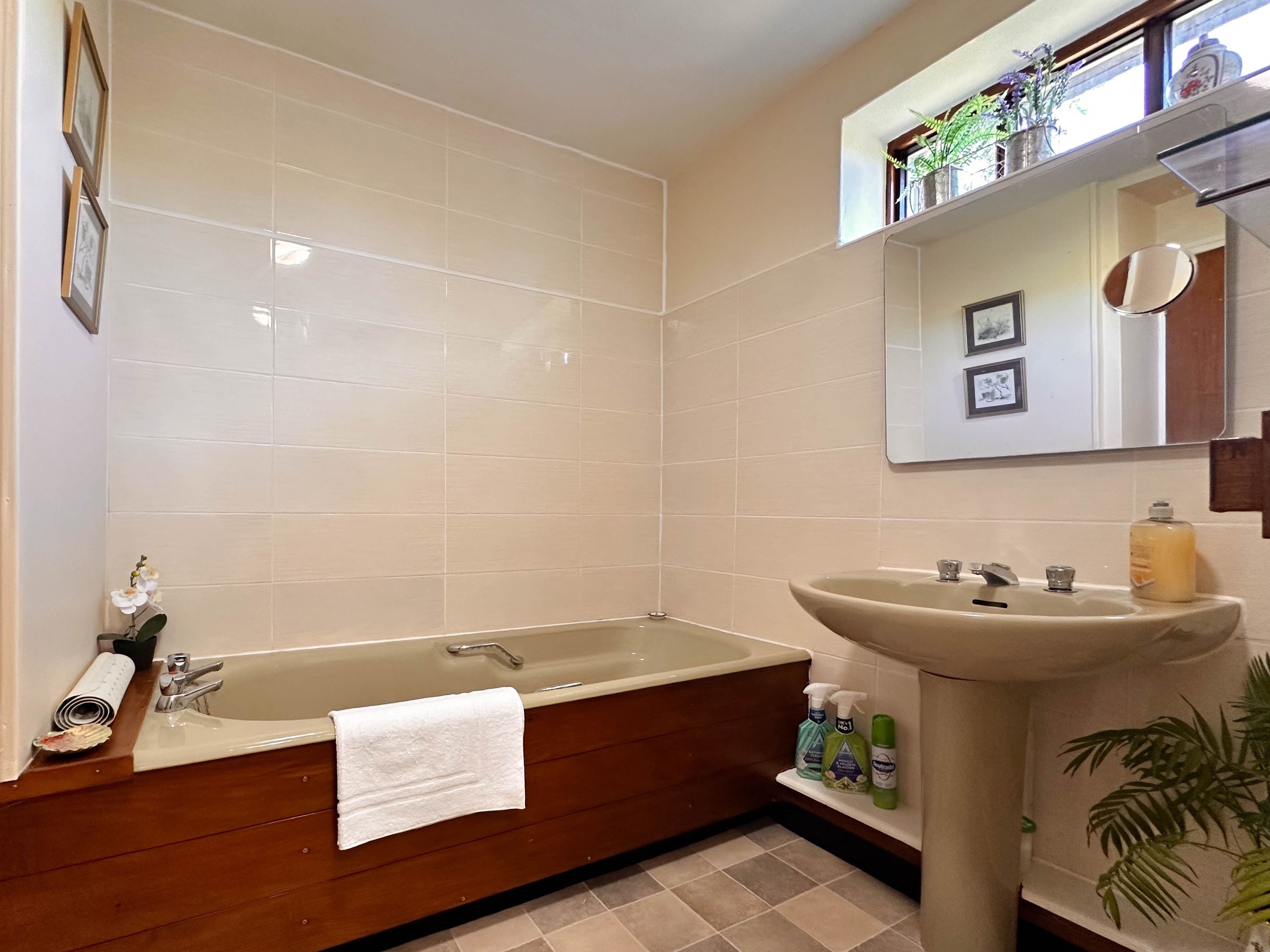 A bathroom with a bathtub, a sink, and a mirror. There are toiletries on the sink and a towel hanging on the bathtub.