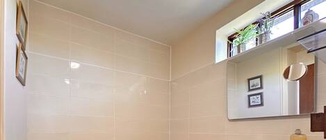 A bathroom with a bathtub, a sink, and a mirror. There are toiletries on the sink and a towel hanging on the bathtub.