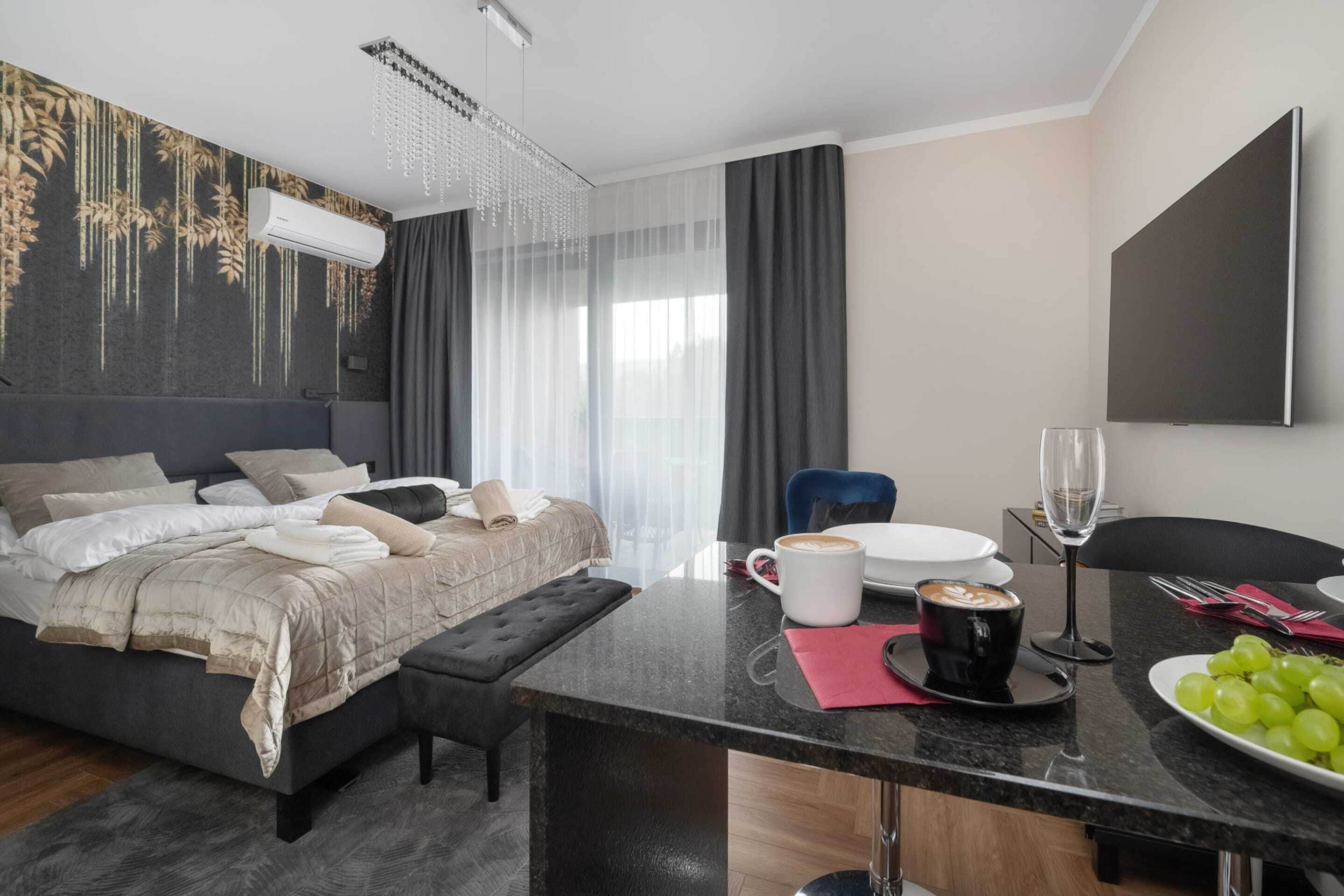 A modern hotel room with a bed, a desk with a coffee cup, a plate of grapes, and a TV.