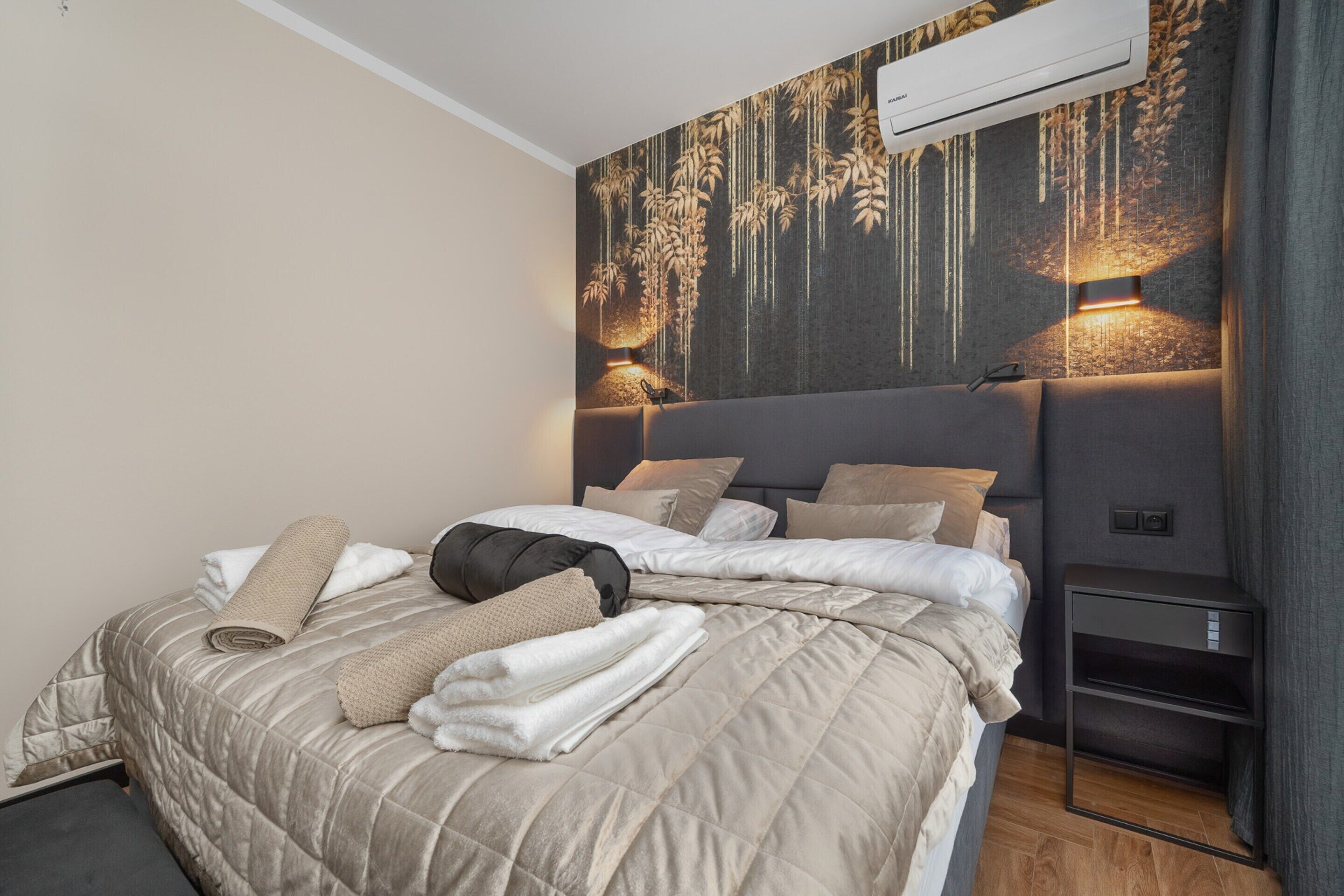 Quarto de hotel moderno com uma cama grande, cabeceira com iluminação vertical e ar condicionado fixado na parede.