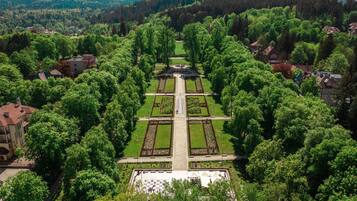 An aerial view of a formal garden with symmetrical pathways, a central fountain, and surrounding trees.