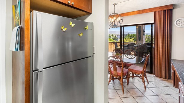 Una cocina con un refrigerador de acero inoxidable, armarios de madera, una zona de comedor con sillas de mimbre y vistas a través de un vidrio.