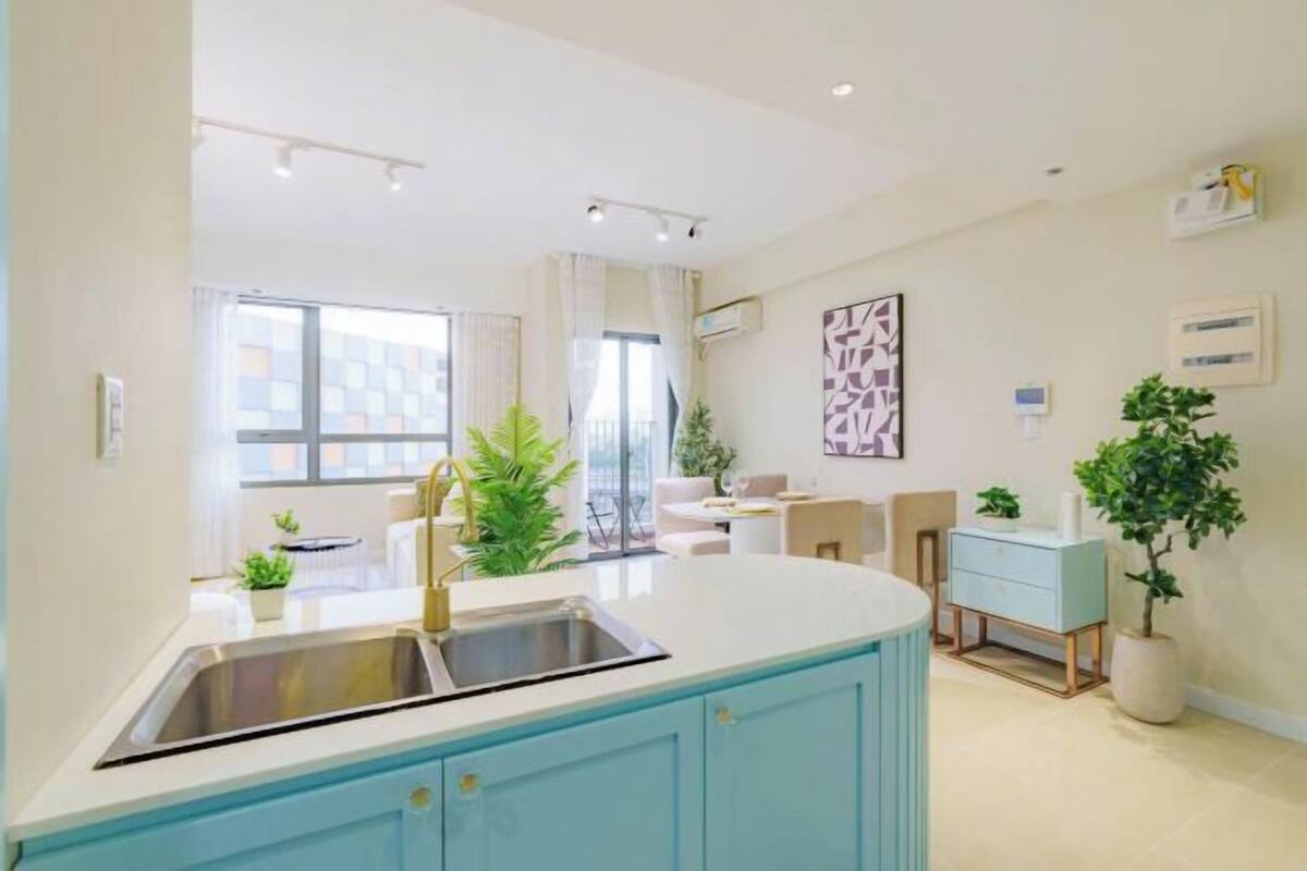 A modern kitchen with a central island, a sink, and a dining area with a light blue cabinet and a white countertop.