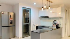 A modern kitchen with a stainless steel refrigerator, a glass door entrance, and a central island with a sink and kettle. - Thao Dien Masteri Riverside - Saigon Home (Ho Chi Minh City)