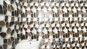 A bathroom with a mosaic tile wall, a white sink, and a shower with a handheld showerhead. - RedDoorz near Politeknik Pariwisata Nusa Dua Bali (Bali)