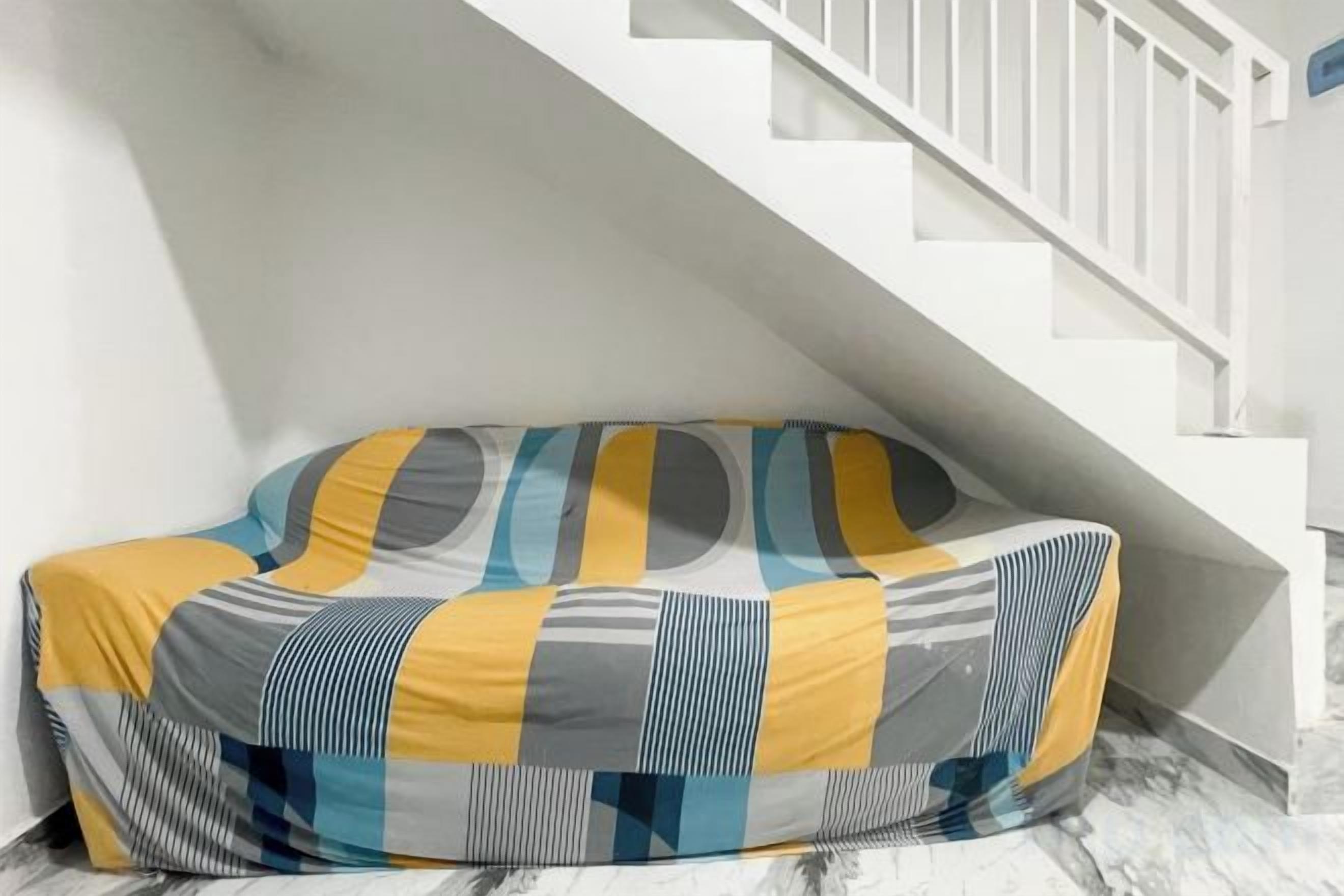 A sofa with a geometric pattern, positioned against a white wall with a staircase in the background.