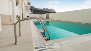 A swimming pool with a metal ladder, surrounded by a white building with balconies.