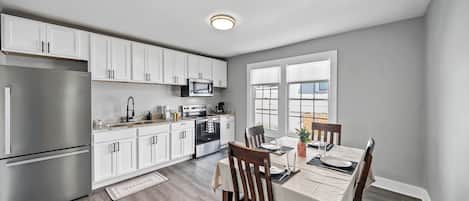 Una cocina moderna con gabinetes blancos, electrodomésticos de acero inoxidable y un comedor con una mesa lista para dos.