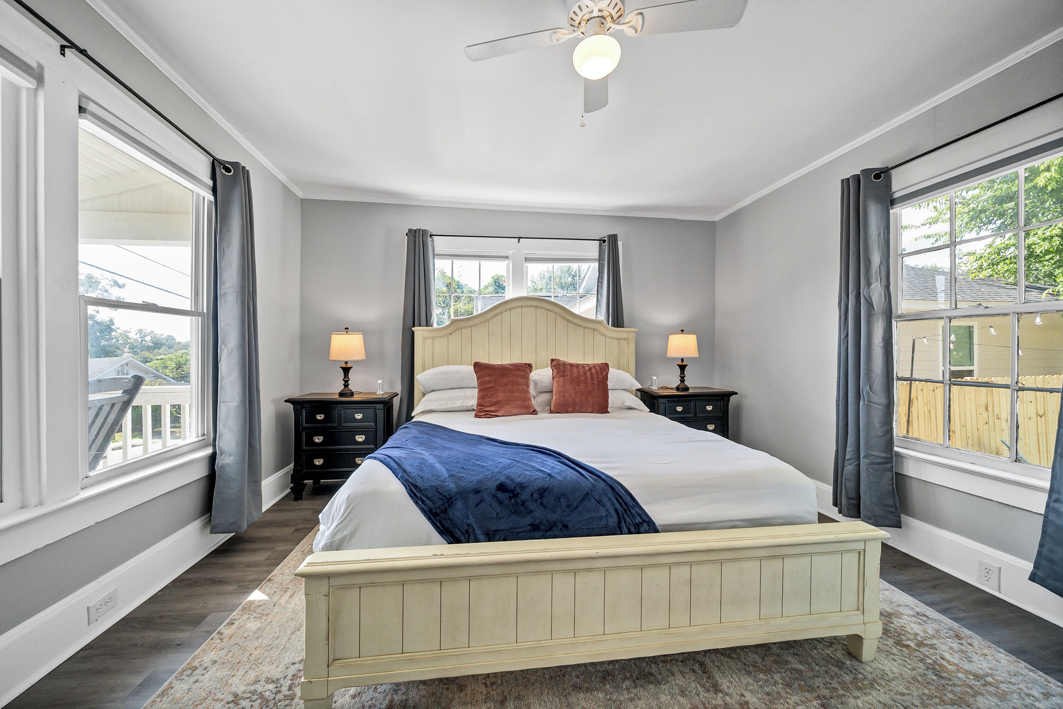 Une chambre à coucher avec un lit, des tables de chevet, un ventilateur de plafond et de grandes fenêtres.