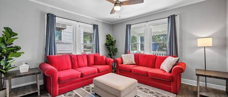 A living room with two red sofas, a beige ottoman, a patterned rug, a ceiling fan, and a lamp.