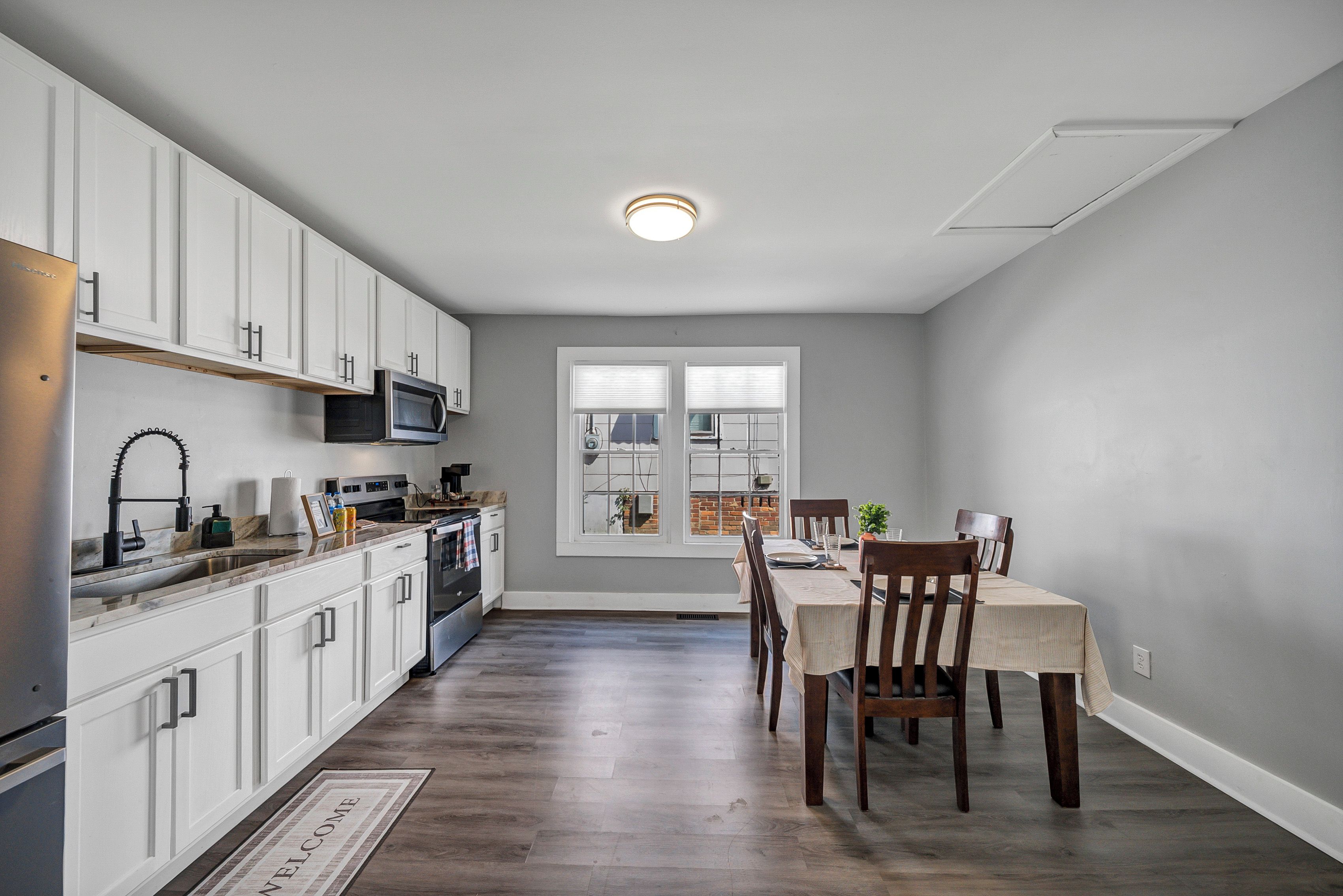 A kitchen with white cabinets, a microwave, and a stove. There is a dining table with chairs and a window with blinds.