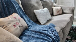 Un sofá gris con una manta azul y cojines estampados.