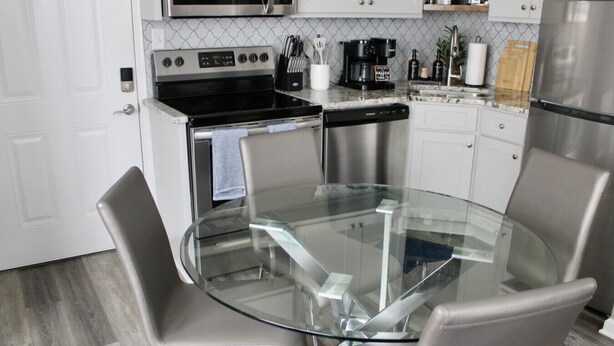 Una cocina moderna con una mesa de comedor de vidrio, electrodomésticos de acero inoxidable y salpicadero de azulejos blancos.