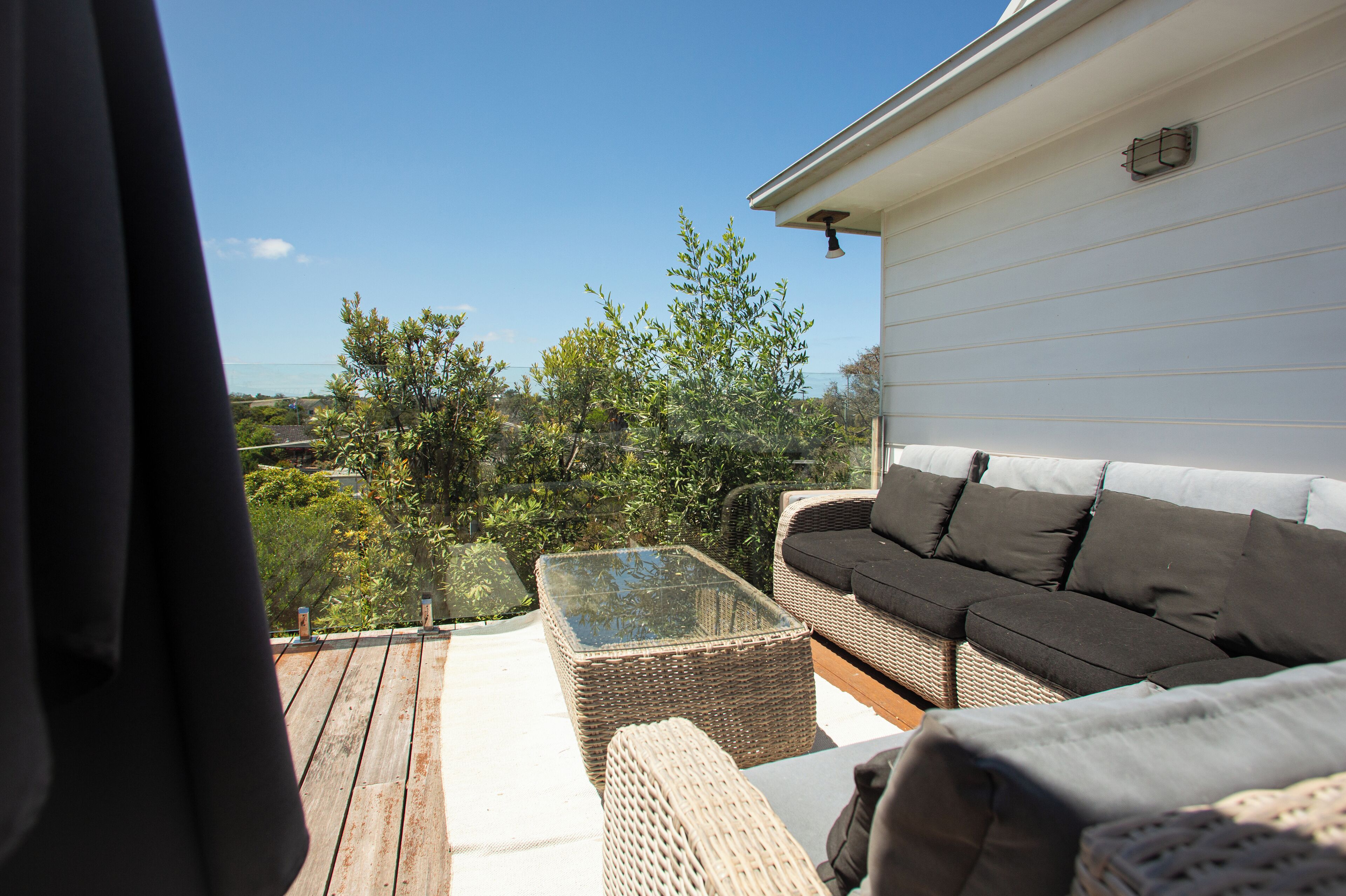 Un patio con muebles de mimbre, una mesa con superficie de vidrio y vistas a árboles y un edificio.