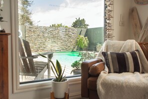 A cozy room with a view of a swimming pool, a comfortable chair, and a potted plant.