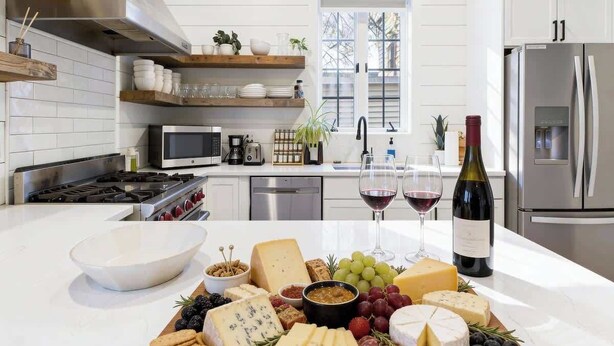 A modern kitchen with white cabinetry, a stainless steel refrigerator, a wooden countertop with a cheese board, and a window providing natural light. - Luxe Chicago Retreat • Game Room, Deck + Fire Pit (Chicago)