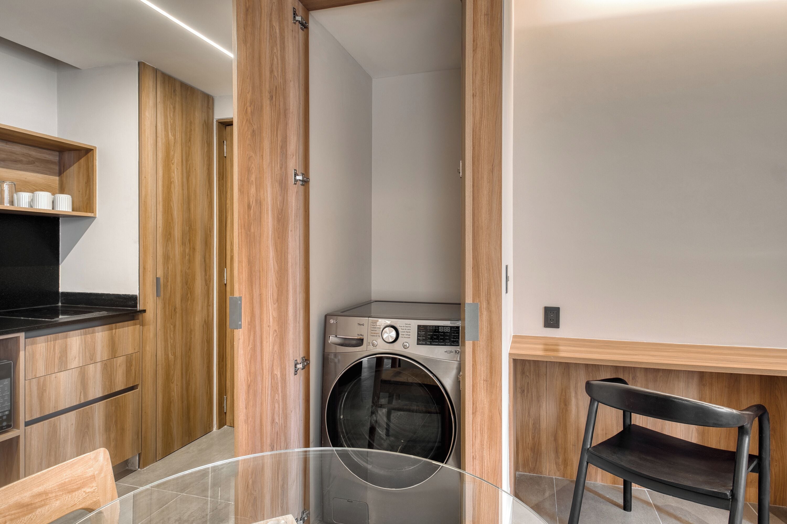A compact kitchen with wooden cabinets, a built-in washing machine, and a glass table.