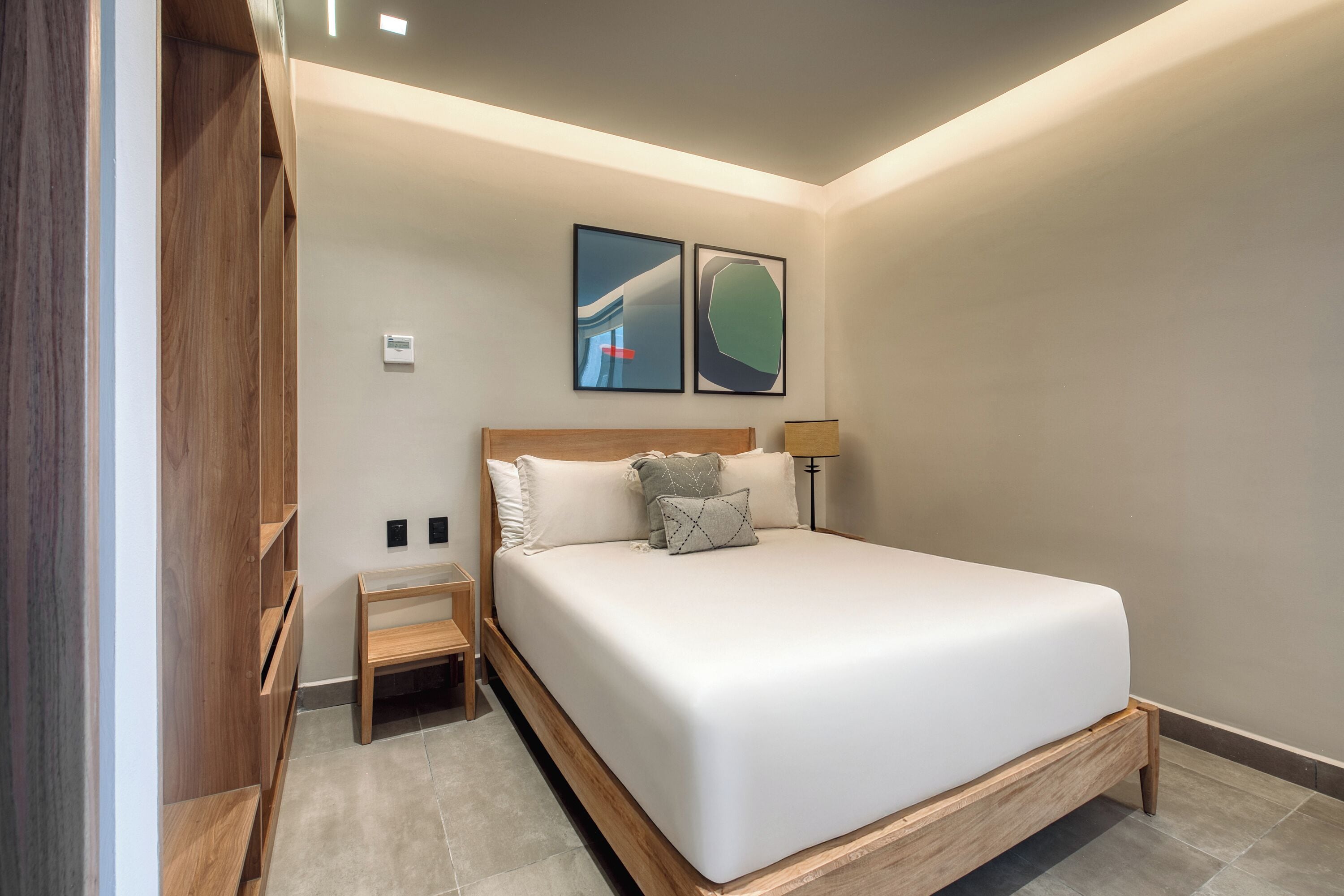 Een moderne slaapkamer met een groot bed, een houten hoofdbord, twee nachtkastjes en twee kunstwerken in een lijst aan de muur.