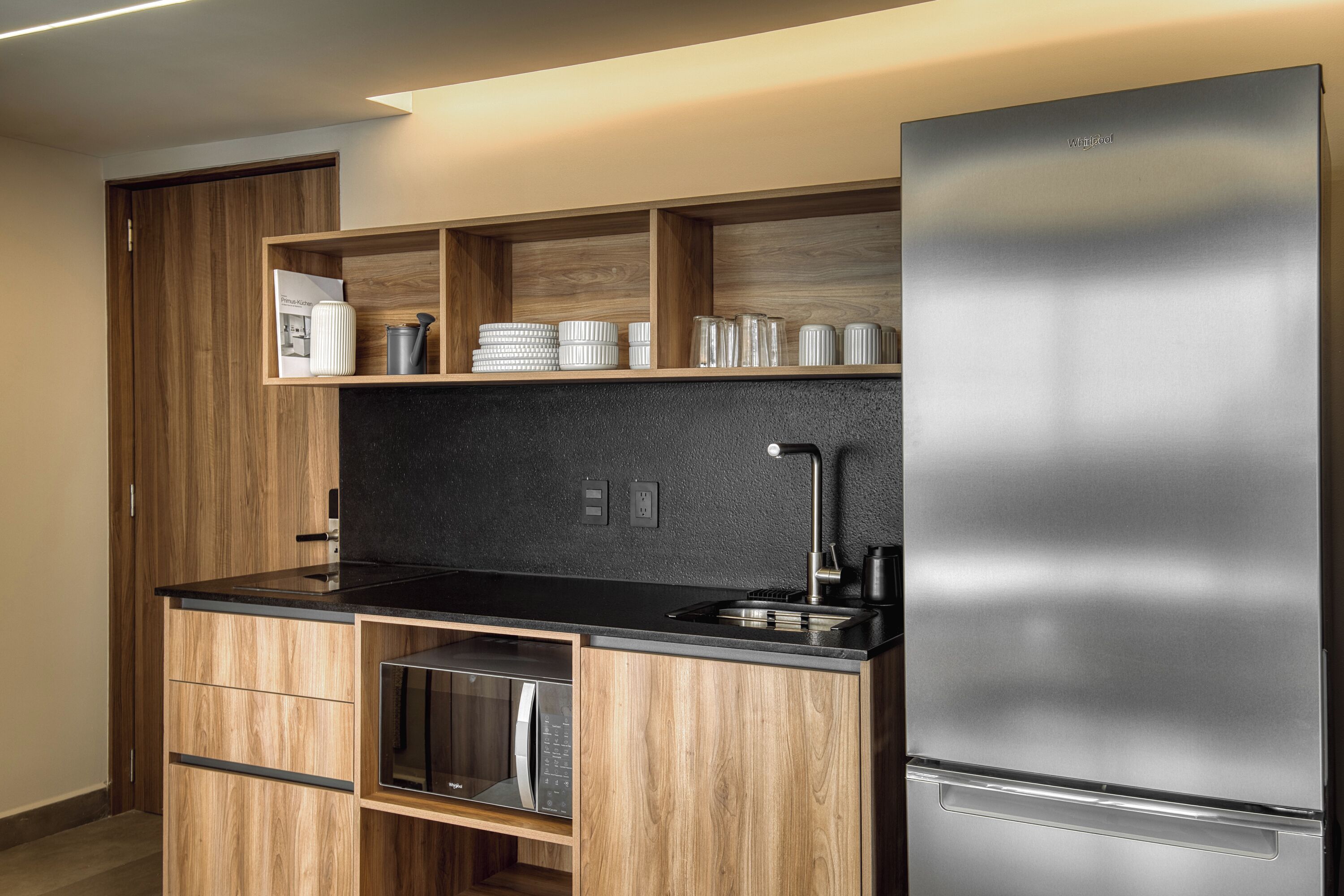 Cocina moderna con armarios de madera, refrigerador de acero inoxidable y encimera negra.