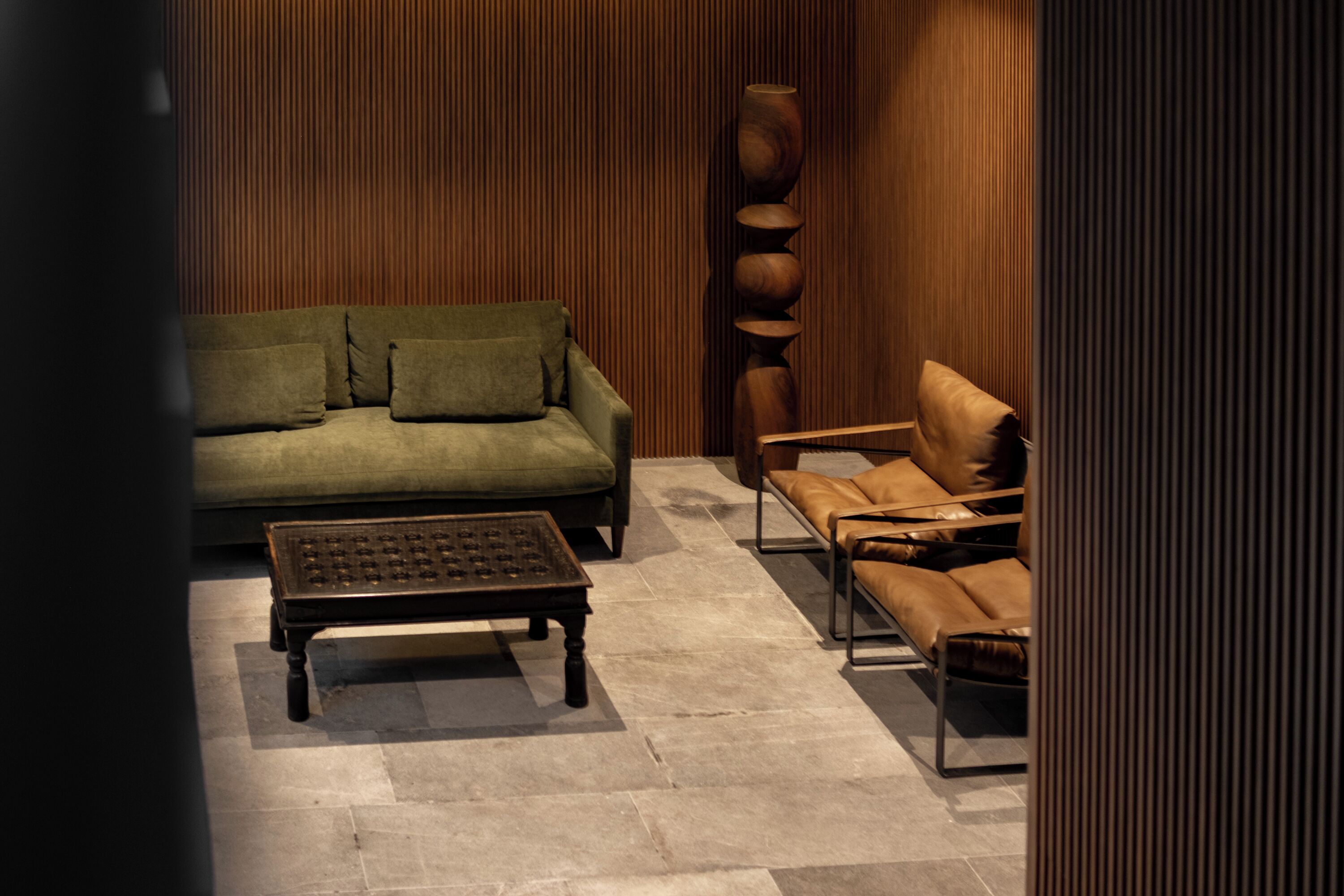A modern living room with a green sofa, a brown leather sofa, a coffee table, and a tall wooden sculpture.