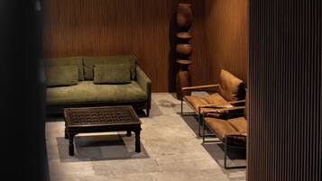 A modern living room with a green sofa, a brown leather sofa, a coffee table, and a tall wooden sculpture.