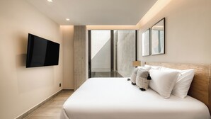 Een moderne hotelkamer met een groot bed, een flatscreen televisie aan de wand en een groot raam met uitzicht op de lucht.