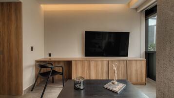 A modern living room with a flat-screen TV mounted on the wall, a wooden cabinet below, a black coffee table with a magazine and a candle, and a black chair.