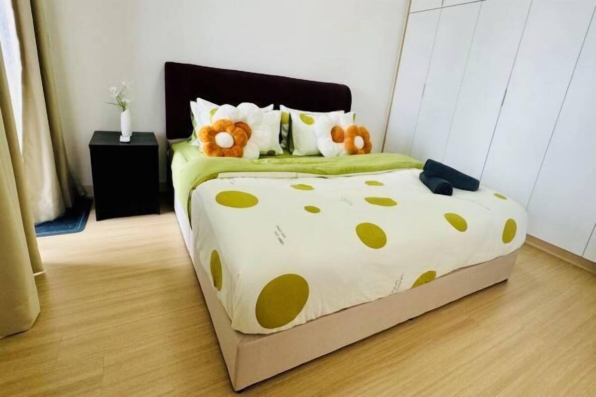 Una cama bien hecha con una colcha de lunares, un cabecero oscuro y una mesita de noche con un florero.