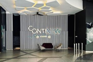 A modern hotel lobby with a black and white striped wall, a reception desk, and a seating area with two chairs. - Continew Residence by Xuan and Partner (Kuala Lumpur)