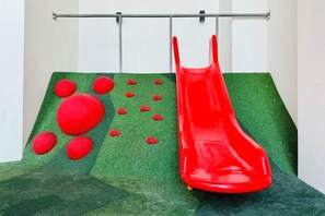 A red slide with a green artificial turf surface and red spherical obstacles. - Continew Residence by Xuan and Partner (Kuala Lumpur)