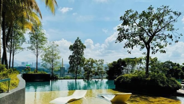 An infinity pool with clear water, surrounded by lush greenery and trees, overlooking a cityscape. - Continew Residence by Xuan and Partner (Kuala Lumpur)